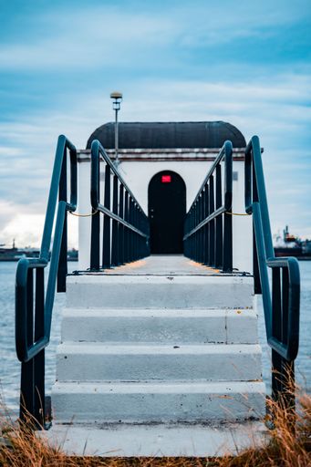 Vertical shot of stone staircase on bridge leading to entrance to observation building on seashore under blue sky