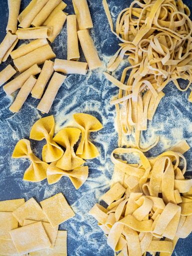 A vertical high angle shot of different types of raw pasta on a table with flour