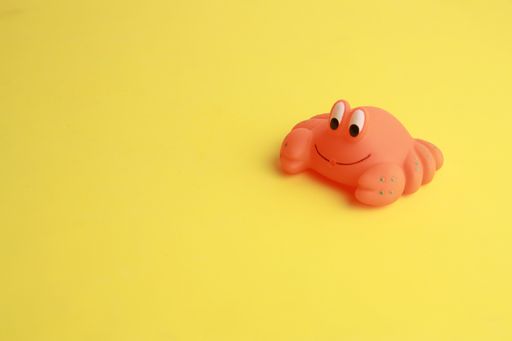 An isolated shot of a small cute crab bathtub toy on a yellow surface
