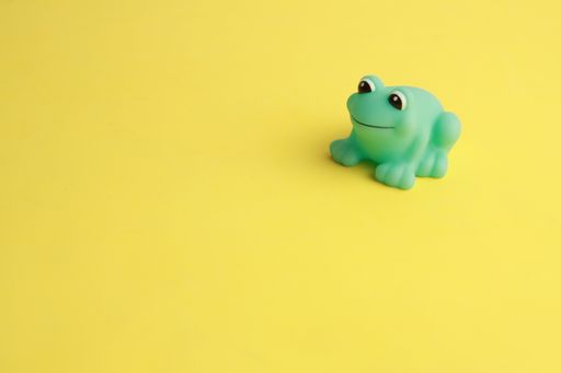 An isolated shot of a small cute green frog bathtub toy on a yellow surface