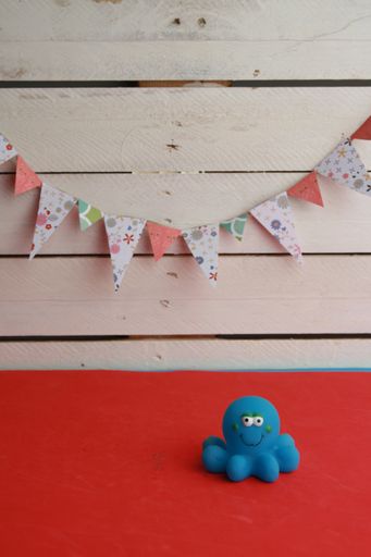 A rubber octopus toy on a red surface with birthday flags hanging from the wooden wall in the background