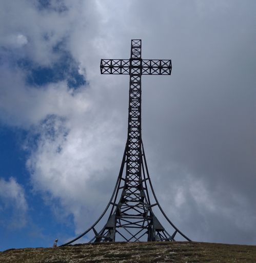 A low angle shot of a huge cross on top of a mountain against cloudy sky in Monte Catria, Italy