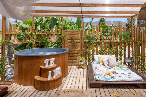 A round-shaped wooden whirlpool bathtub and a bed in a wooden gazebo decorated with exotic plants