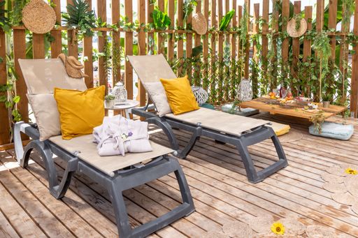 A hanging wooden table and sun loungers in a wooden gazebo decorated with tropical plants