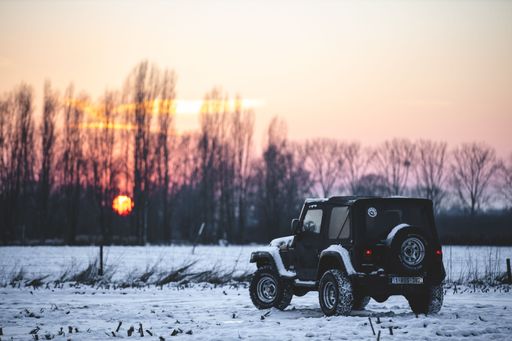 A Jeep wrangler covered in snow at sunset on a cold winter day