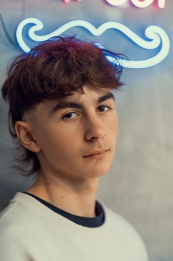 A vertical shot of a young male with styled hair standing on the background of a mustache light