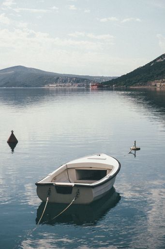 A sailboat moored in a tranquil lake with a buoy tied to its bow.