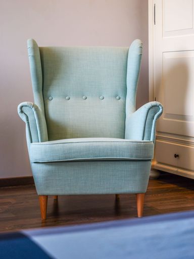 A vertical shot of a pastel green antique armchair seat near a blue rug in a bedroom