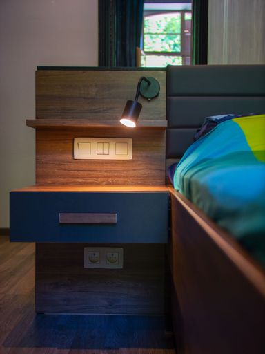 A vertical shot of a wooden bedside table with an illuminated lamp and black drawers