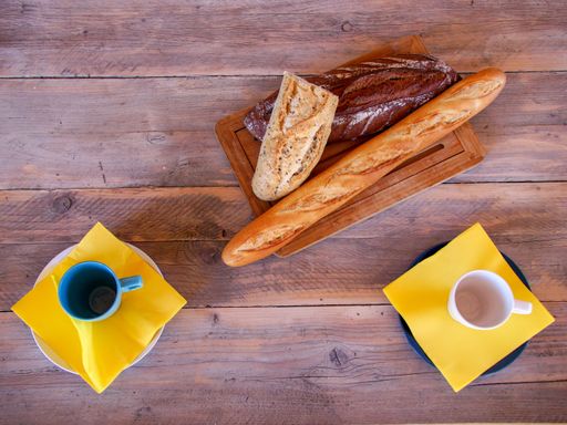 A top view on the wooden table with two cups on yellow napkins and a board of three different buns