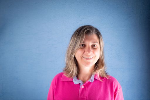 A portrait of a middle-aged Caucasian woman smiling in a pink shirt against a blue background