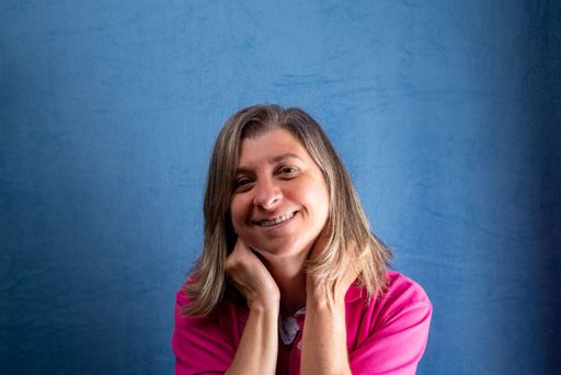 A portrait of a middle-aged Caucasian woman smiling happily in a pink shirt against a blue background