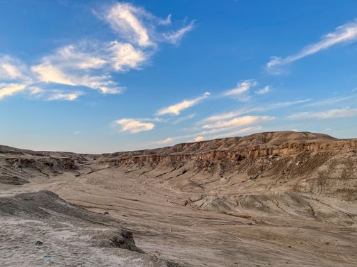A dry landscape of a desert under a blue cloudy sky on a sunny day