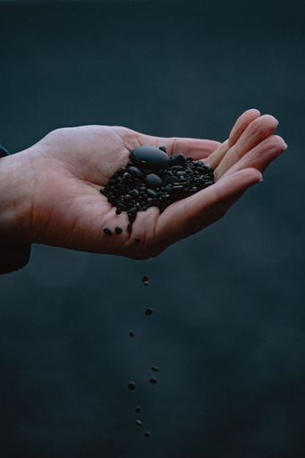 A vertical closeup shot of a hand holding a pile of small rocks with some of them dropping down on a blur background