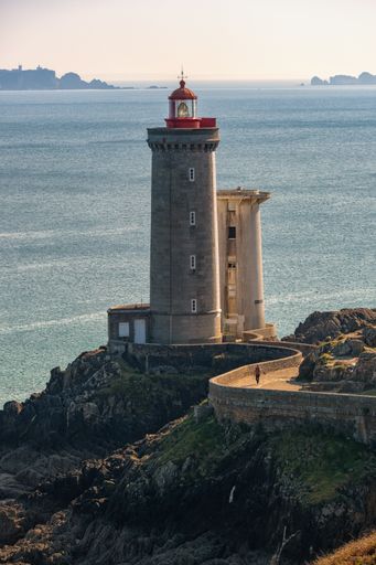 A white concrete lighthouse on the top of a rocky hill near the sea under the clear sky