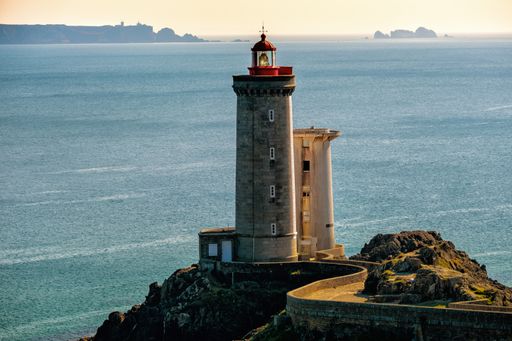 A white concrete lighthouse on the top of a rocky hill near the sea under the clear sky