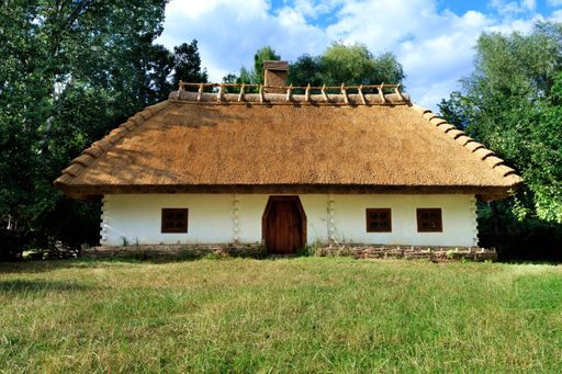 A traditional Ukrainian rural house with a thatched roof and a wicker fence with a green garden