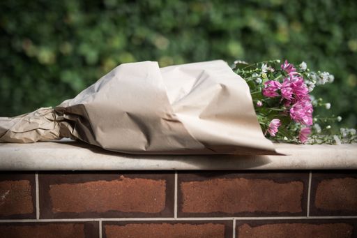 A bouquet of pink wildflowers wrapped in paper on a stone wall