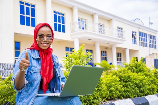 An African female gesturing the like sign while sitting in the park with her laptop