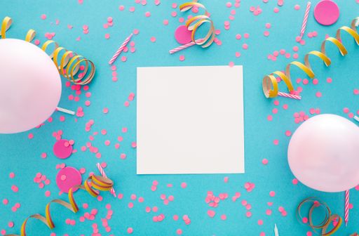 A top view of a blank square paper surrounded by balloons and confetti on a blue background