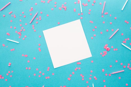 A top view of a blank square paper surrounded by confetti on a blue background