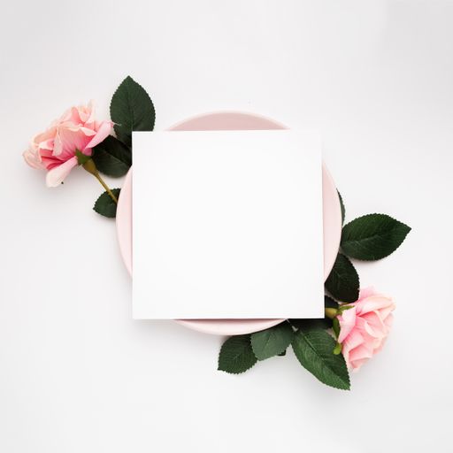 A blank piece of paper on a pink plate surrounded by roses isolated on a white background