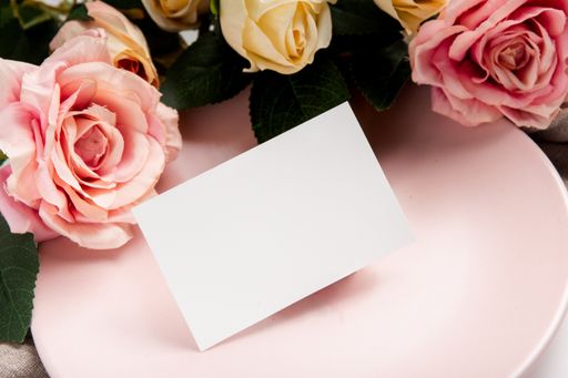 A blank piece of paper on a pink plate surrounded by roses isolated on a white background