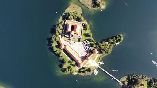 An aerial shot of Trakai Island Castle surrounded by green trees in the heart of Lake Galva