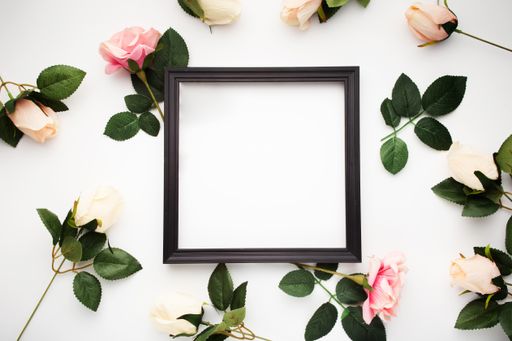 A top view of a black square frame surrounded by roses isolated on a white background