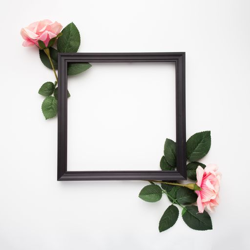 A top view of a black square frame surrounded by roses isolated on a white background