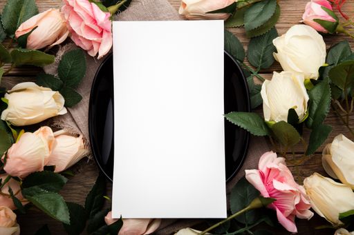 A blank piece of paper surrounded by roses on a wooden surface