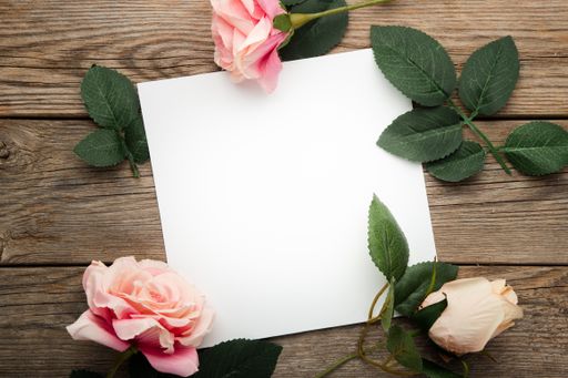A blank piece of paper surrounded by roses on a wooden surface