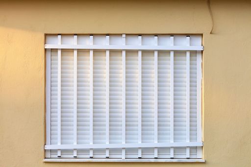 White blinds covered by a metallic fence on a golden-colored wall