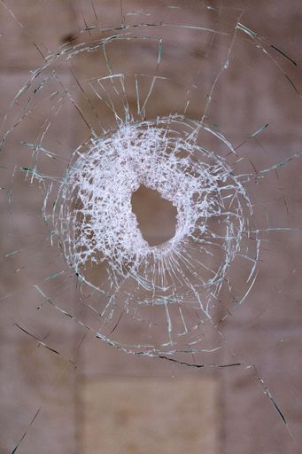 A vertical closeup of glass shattered by a bullet on a dark beige background