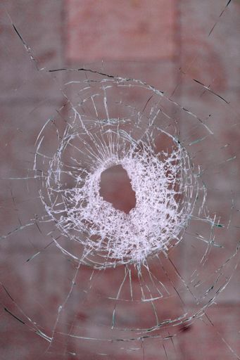 A vertical closeup of glass shattered by a bullet on a dark beige background
