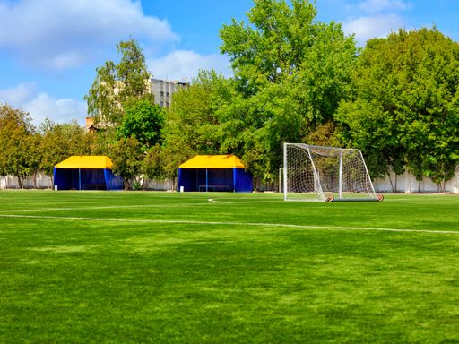 The green lawn of a football field with gates, netting and tents on a summer day against a green foliage