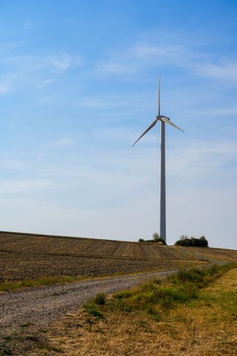 A vertical shot of tall wind turbine in the field on blue sky background