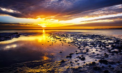 A landscape with ocean waves hitting a rocky coast during sunset