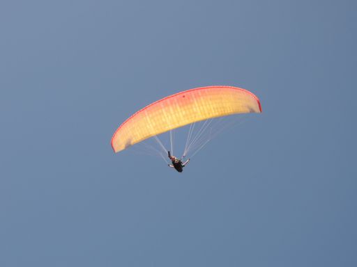 A person paragliding in a free fly in Europe in Alps mountains with blue sky in the background