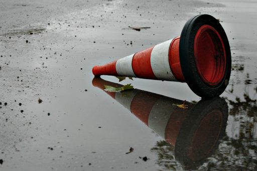 A striped traffic cone dropped on shallow puddle in the street