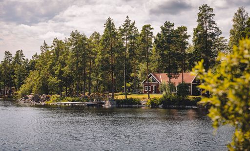A breathtaking scenery of a forest landscape with a wooden house and high trees near the lake shore