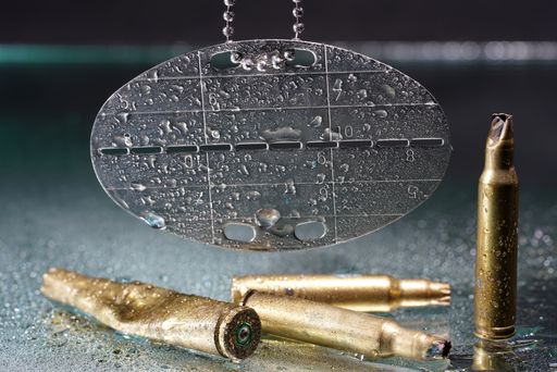 A closeup shot of ammunition and a metal dog tag with waterdrops