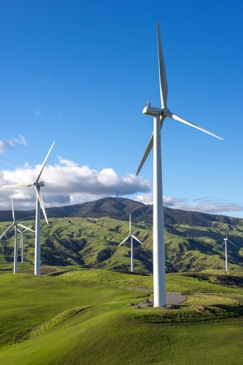 Tall wind turbines in a green meadow with mountains in the background