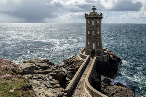 A high angle shot of a concrete lighthouse on a rock formation near the sea during daytime