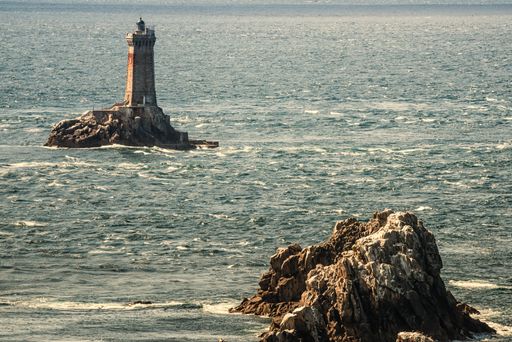 A concrete lighthouse on a rock formation in the middle of the sea during daytime