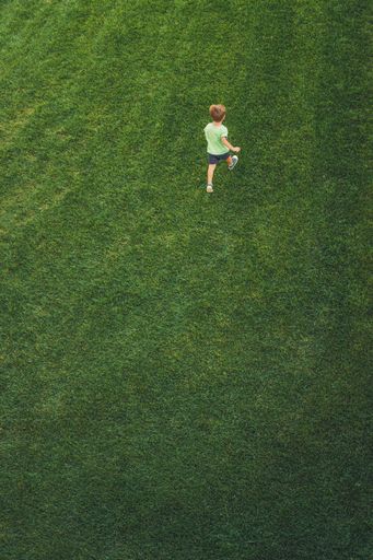 A vertical shot of a little boy running and playing on a field full of grass