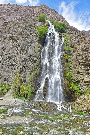 A vertical shot of a waterfall flowing down the cliff under the blue sky