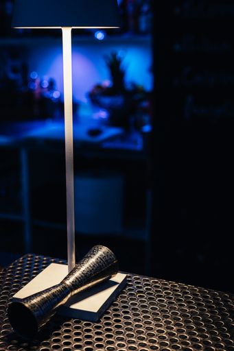 The vertical high-angle shot of a jigger under the light of a lamp on a bar counter
