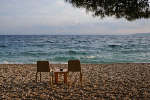 The two chairs and small table on the sandy beach facing the sea