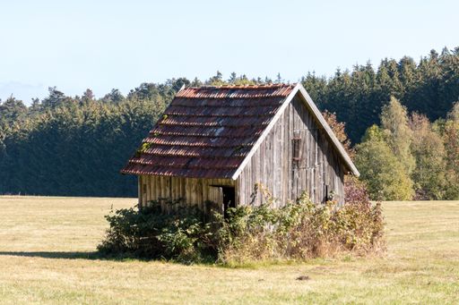 A scenic view of a small house built in an open field with a tree line in the background
